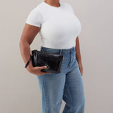Person wearing a white t-shirt and blue jeans holding a black clutch against a neutral background