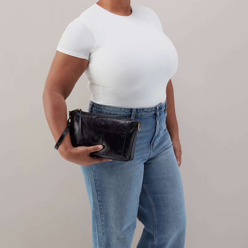 Person wearing a white t-shirt and blue jeans holding a black clutch against a neutral background