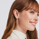 Close-up of a woman wearing gold hoop earrings with a plain background