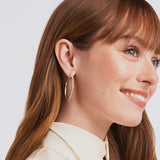 Close-up of a woman wearing gold hoop earrings with a plain background