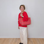 Woman in red sweater holding a red patterned bag against a white wall.