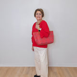 Woman in red sweater holding a red patterned bag against a white wall.