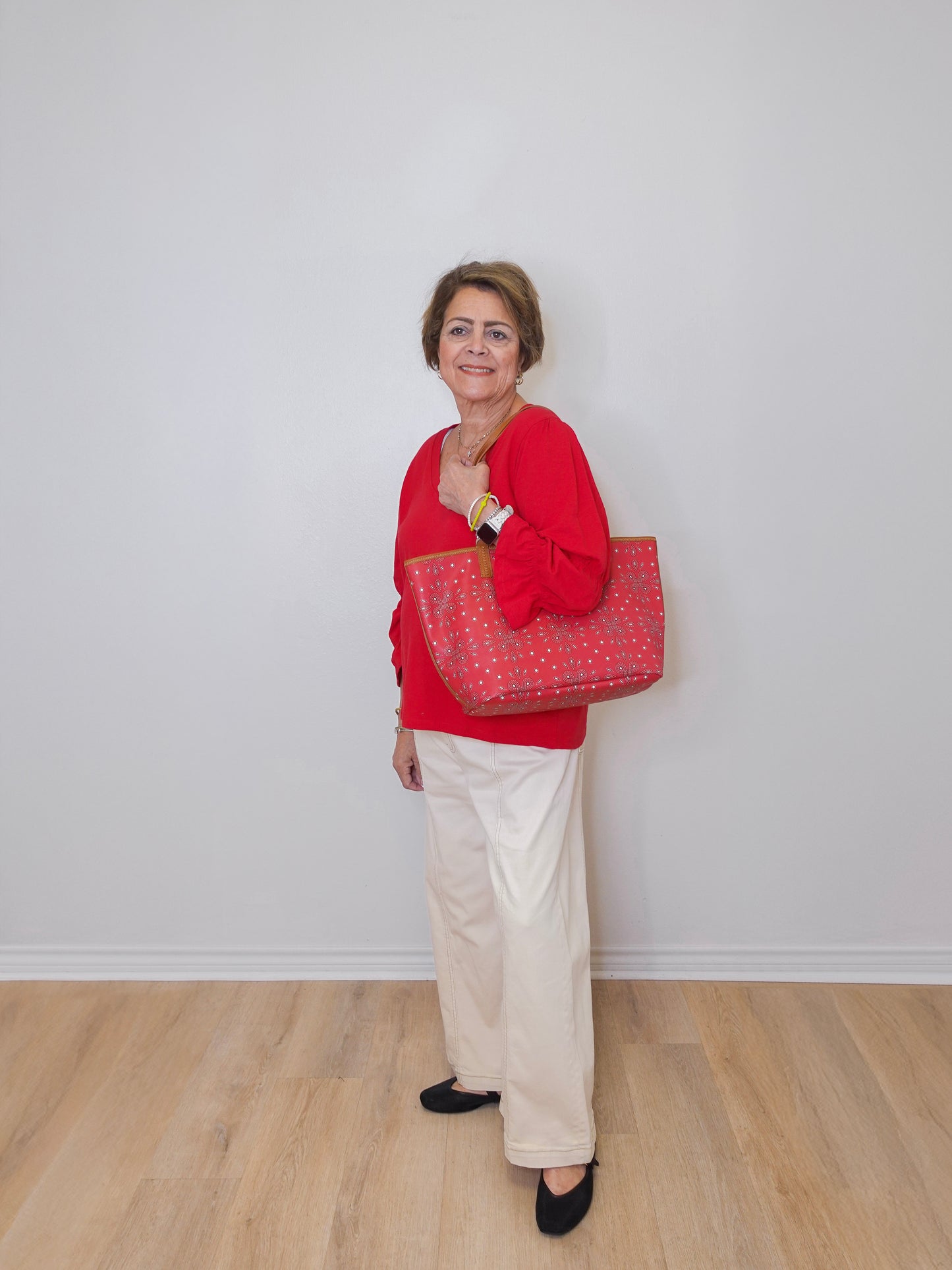 Woman in red sweater holding a red patterned bag against a white wall.