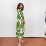 Woman wearing a green dress with white patterns against a white wall.
