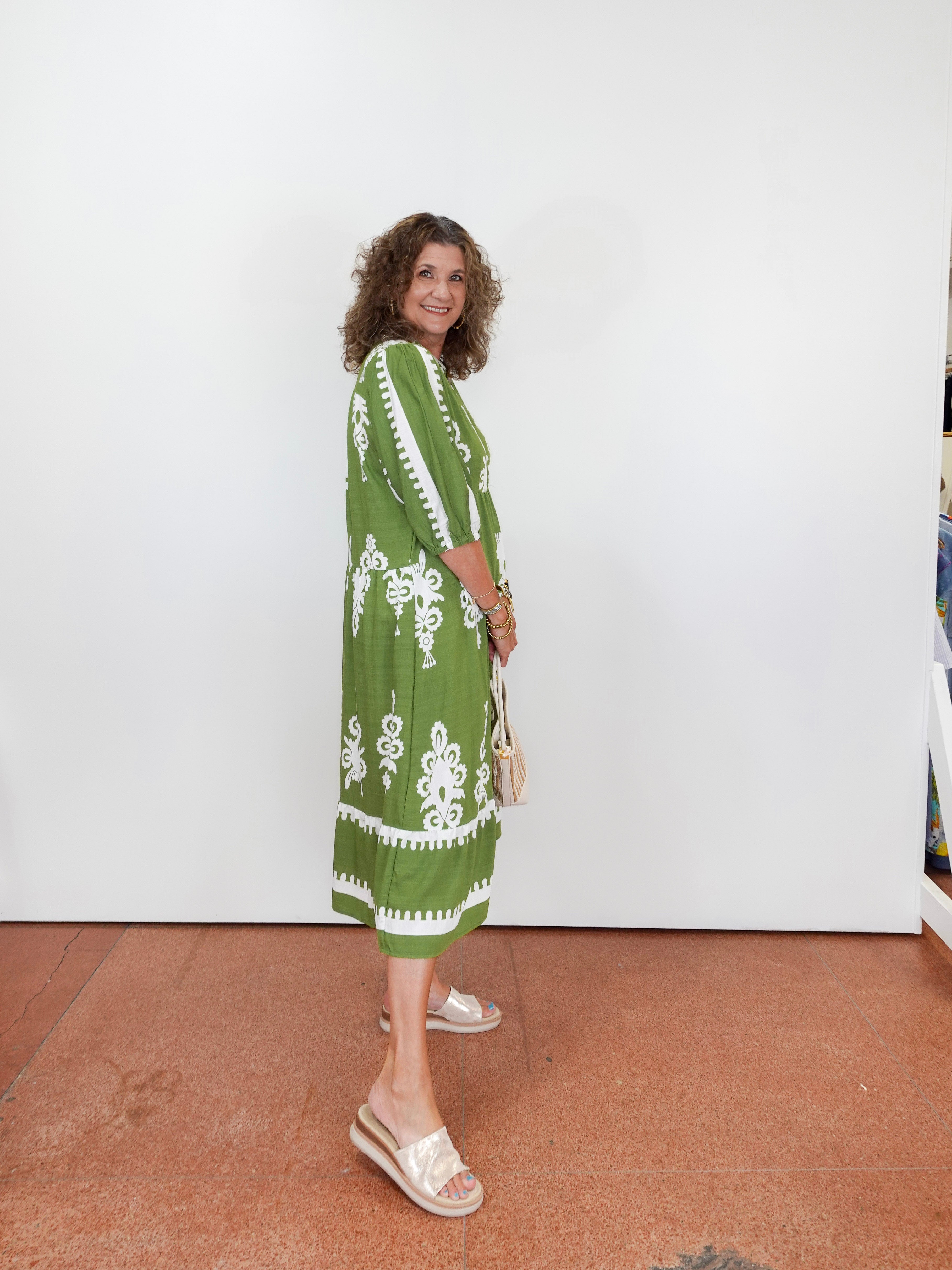 Woman wearing a green dress with white patterns against a white wall.
