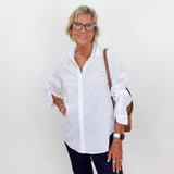 Woman wearing a white shirt and dark pants against a white wall