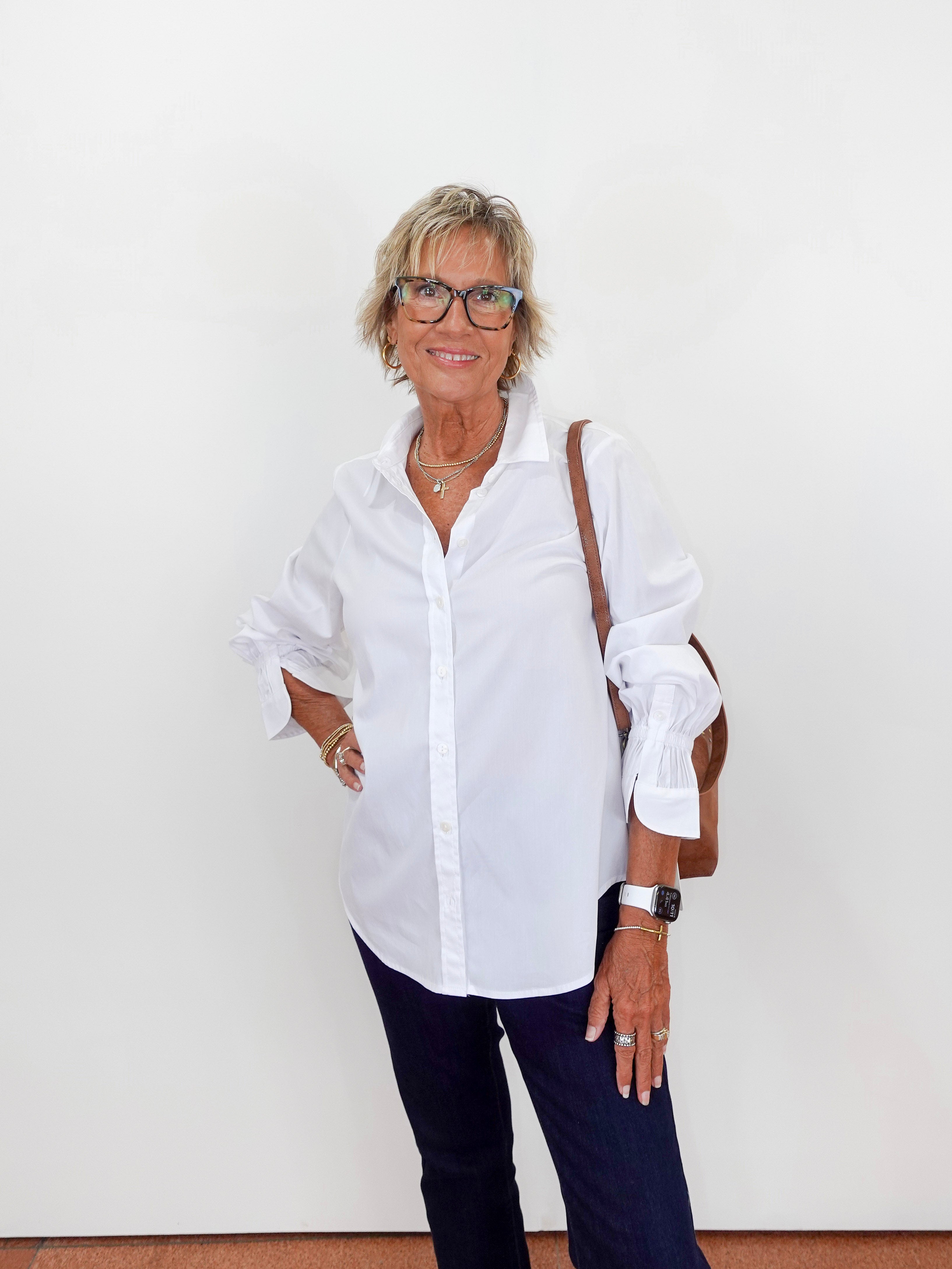 Woman wearing a white shirt and dark pants against a white wall