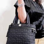 Person holding a black quilted handbag against a neutral background