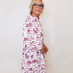 Woman wearing a white dress with red patterns against a plain background