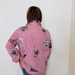 Person wearing a red and white striped shirt with black designs against a white wall