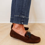 Brown suede loafers worn with rolled-up jeans on a light wooden floor.