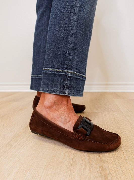 Brown suede loafers worn with rolled-up jeans on a light wooden floor.