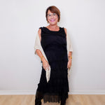 Woman wearing a black dress with sheer sleeves against a white wall