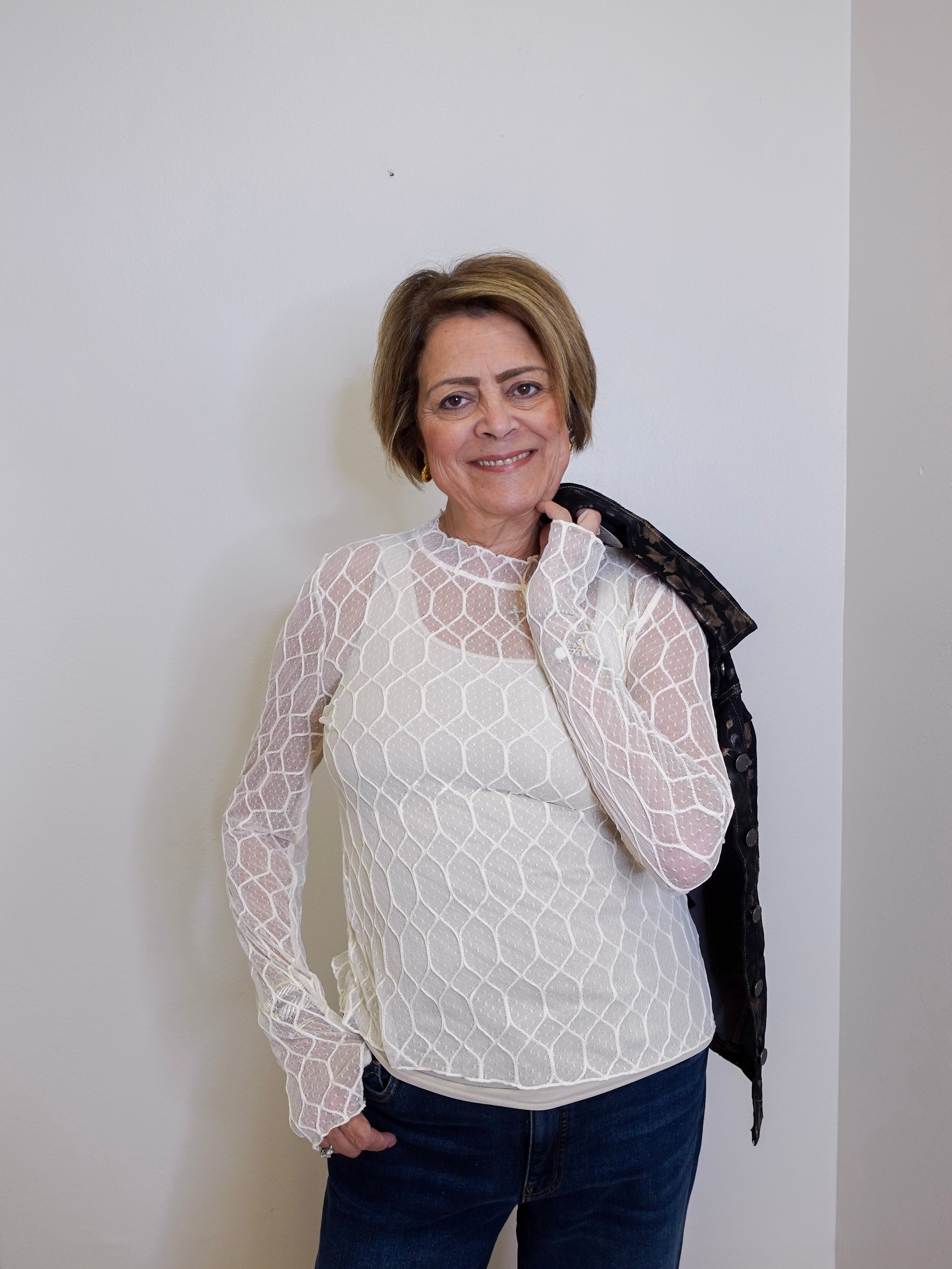Woman wearing a white lace top and dark pants against a plain background