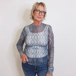 Woman wearing a sheer long-sleeve top with a geometric pattern against a plain background