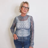 Woman wearing a sheer long-sleeve top with a geometric pattern against a plain background