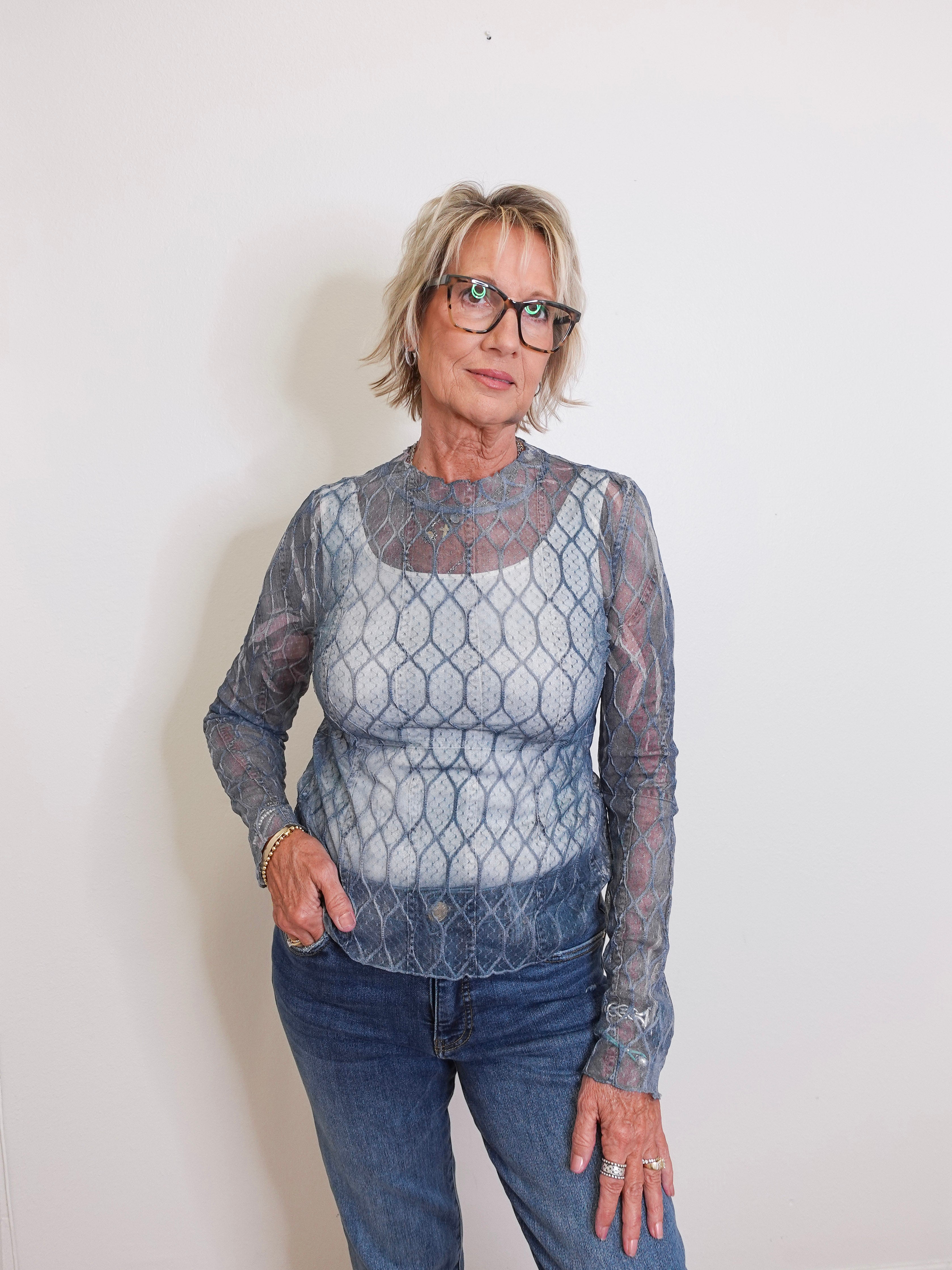 Woman wearing a sheer long-sleeve top with a geometric pattern against a plain background