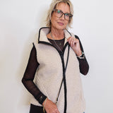 Woman wearing a cream sherpa vest over a black top with a white background