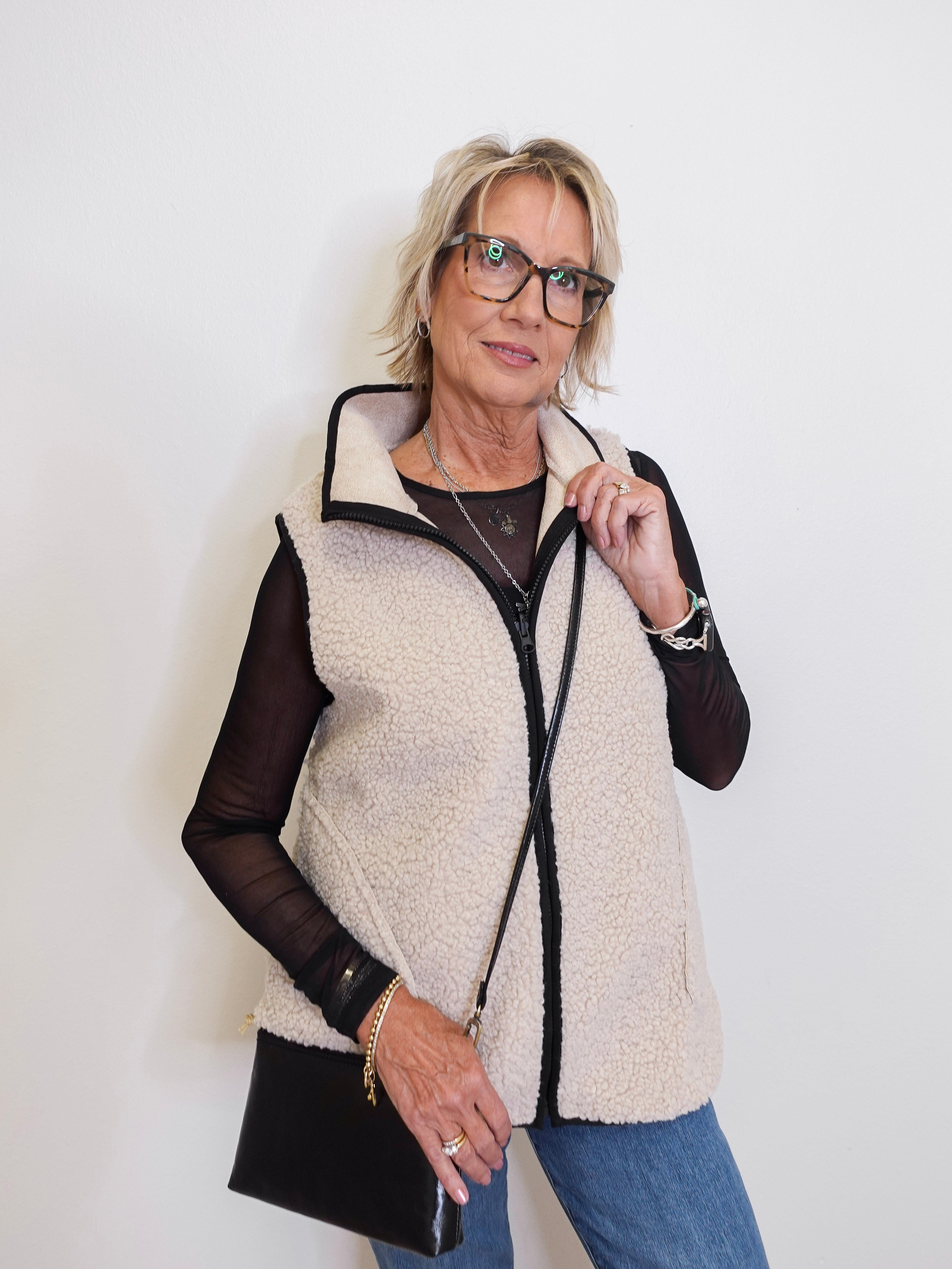 Woman wearing a cream sherpa vest over a black top with a white background