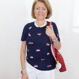 Woman wearing a navy blue top with small flag patterns, holding a red bag against a white background