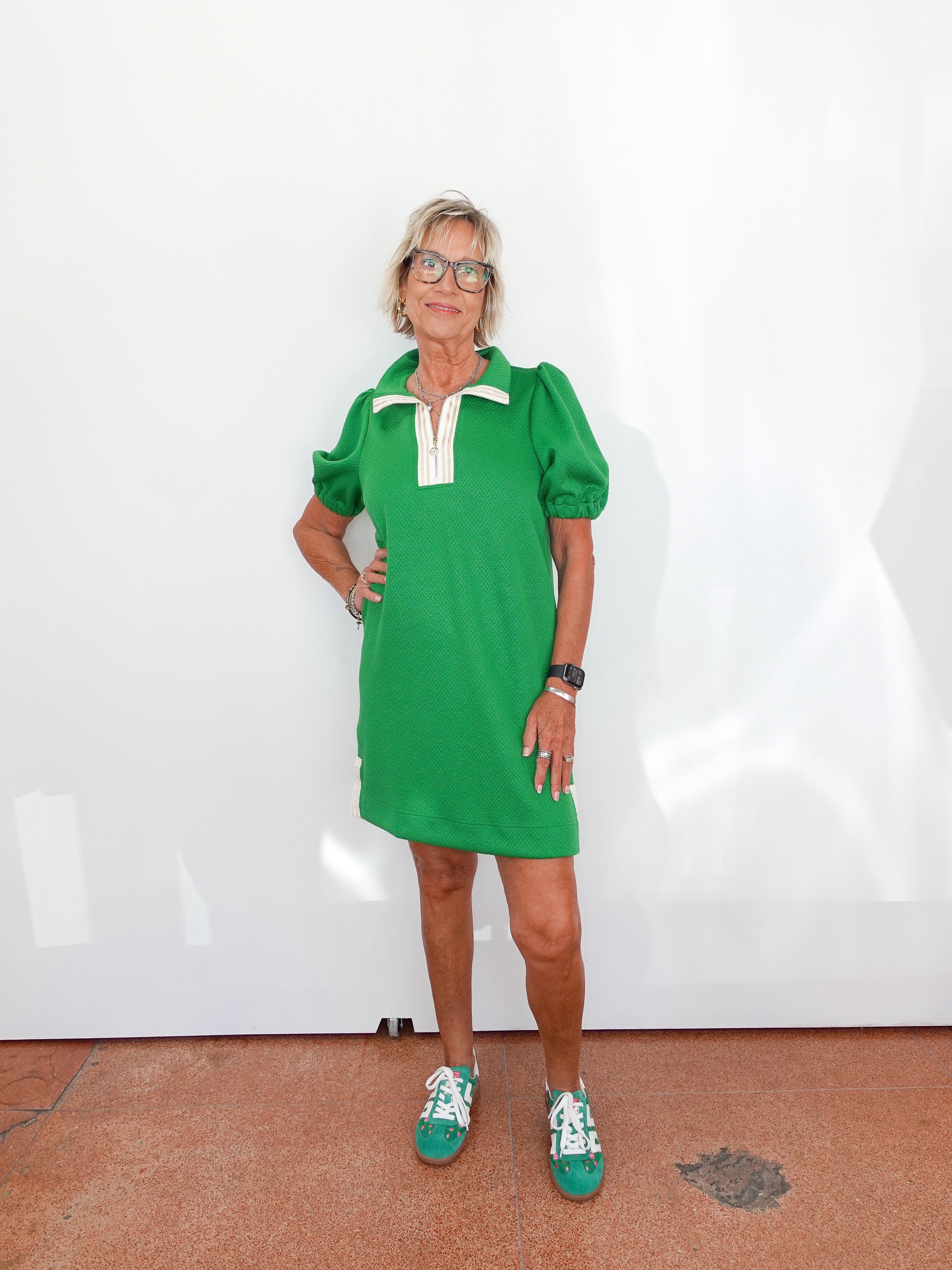 Woman wearing a green dress with white collar and cuffs, standing against a plain white background.