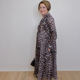 Woman wearing a leopard print dress with Adidas shoes against a white wall.