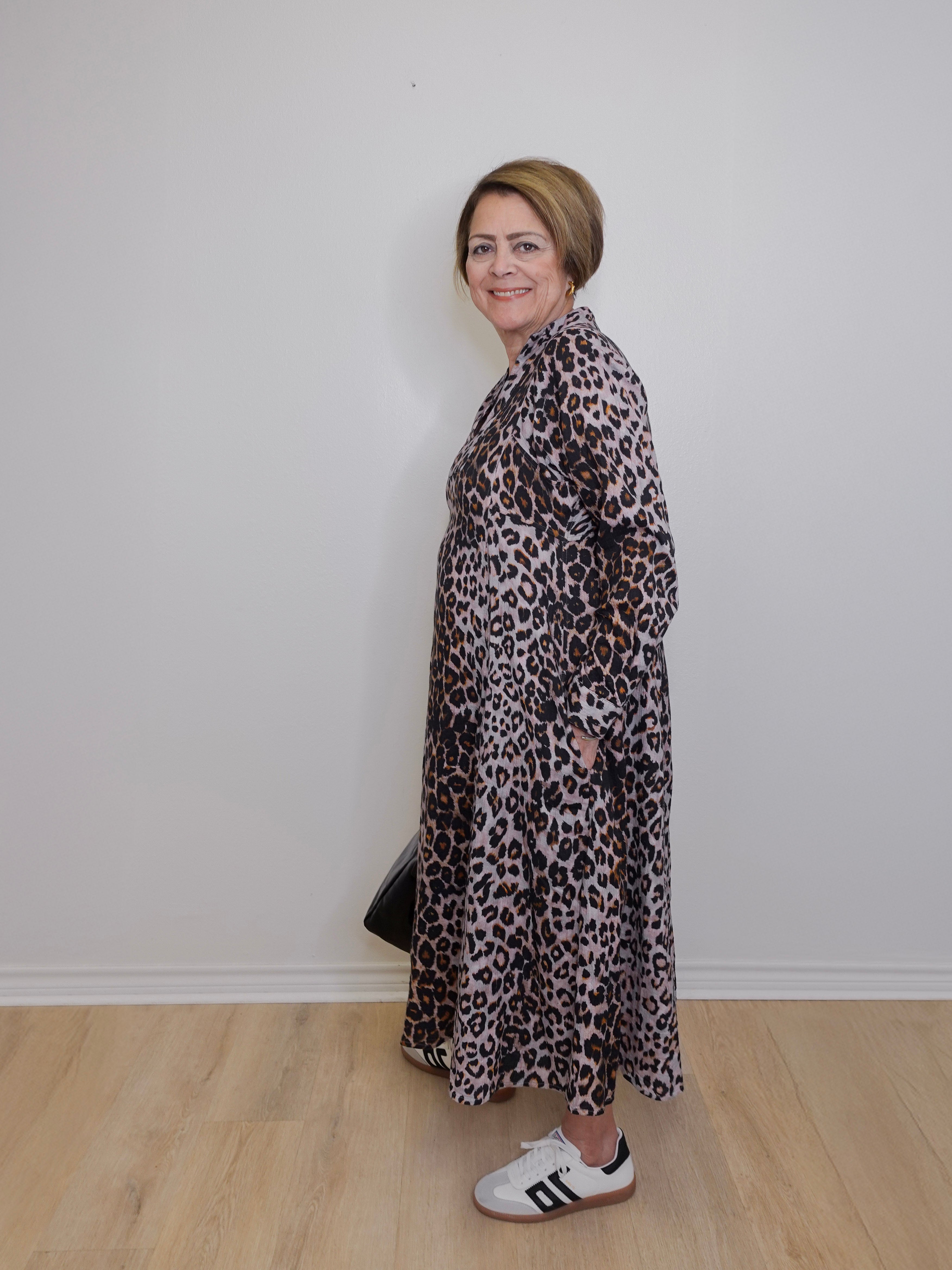 Woman wearing a leopard print dress with Adidas shoes against a white wall.