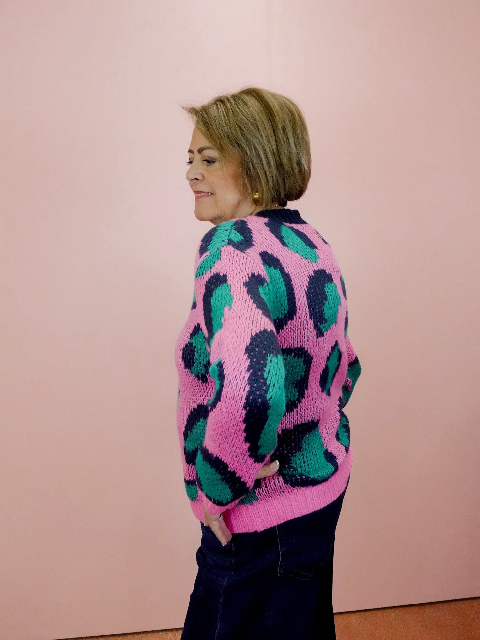 Person wearing a colorful sweater with a pink and green pattern against a plain background