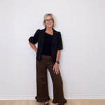 Woman wearing a black blazer and patterned pants against a white wall