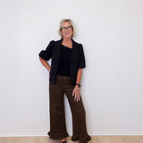 Woman wearing a black blazer and patterned pants against a white wall