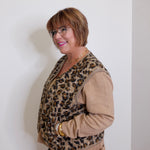 Person wearing a leopard print vest over a beige sweater against a white wall