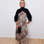 Woman wearing a black turtleneck and leopard print dress against a white wall.