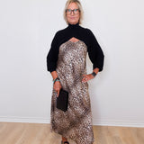 Woman wearing a black turtleneck and leopard print dress against a white wall.