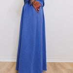 Person wearing a long blue dress with white shoes on a plain background