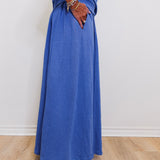 Person wearing a long blue dress with white shoes on a plain background