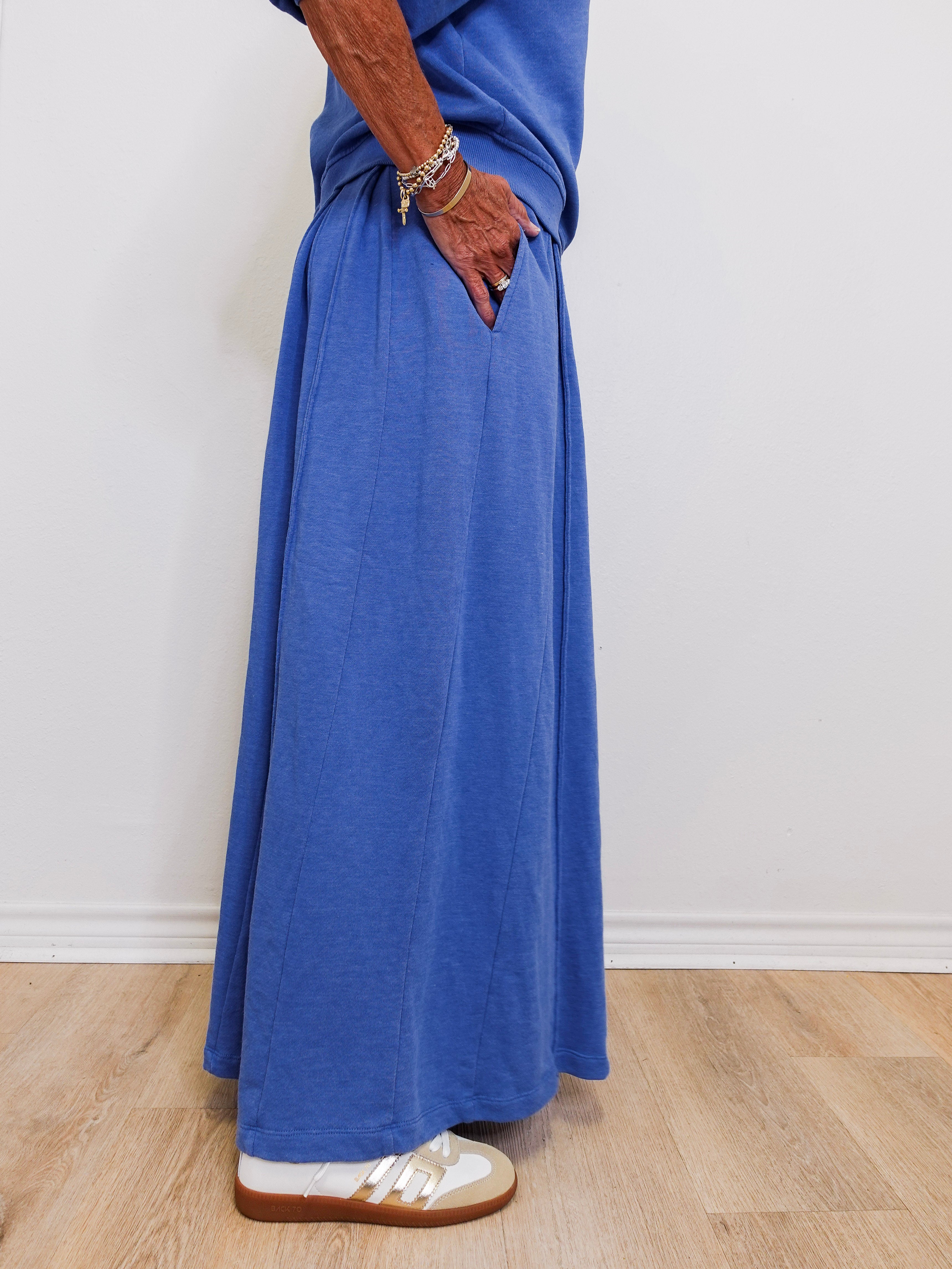 Person wearing a long blue dress with white shoes on a plain background