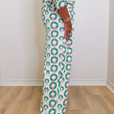 Person wearing a festive pajama set with wreath and bow pattern on a wooden floor.