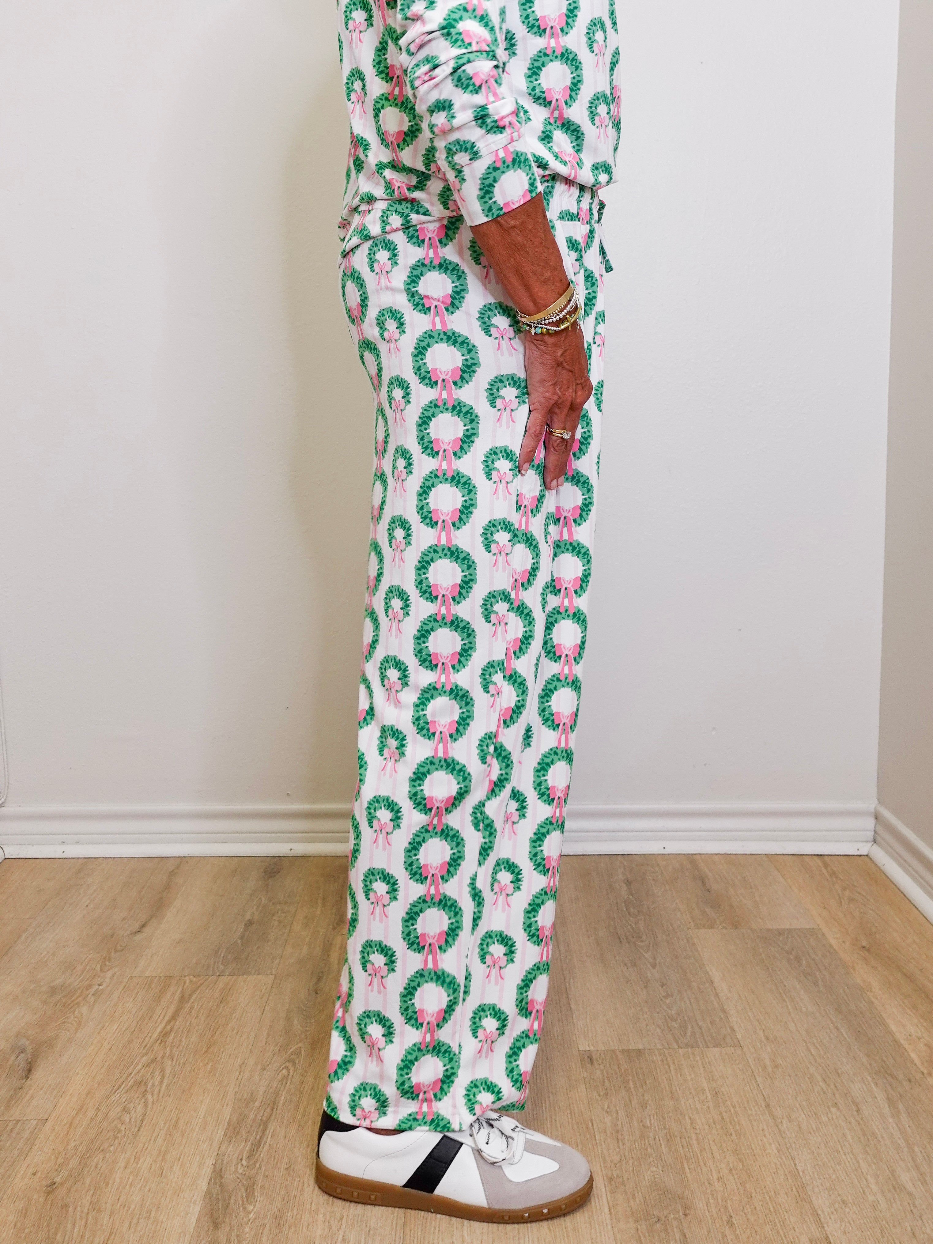 Person wearing a festive pajama set with wreath and bow pattern on a wooden floor.