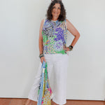 Woman wearing a colorful sleeveless top and white pants, holding a patterned scarf.