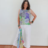 Woman wearing a colorful sleeveless top and white pants, holding a patterned scarf.