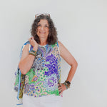 Woman wearing a colorful sleeveless top with a pattern, holding a blue scarf against a white background.