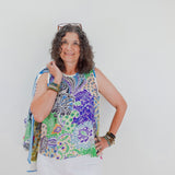 Woman wearing a colorful sleeveless top with a pattern, holding a blue scarf against a white background.