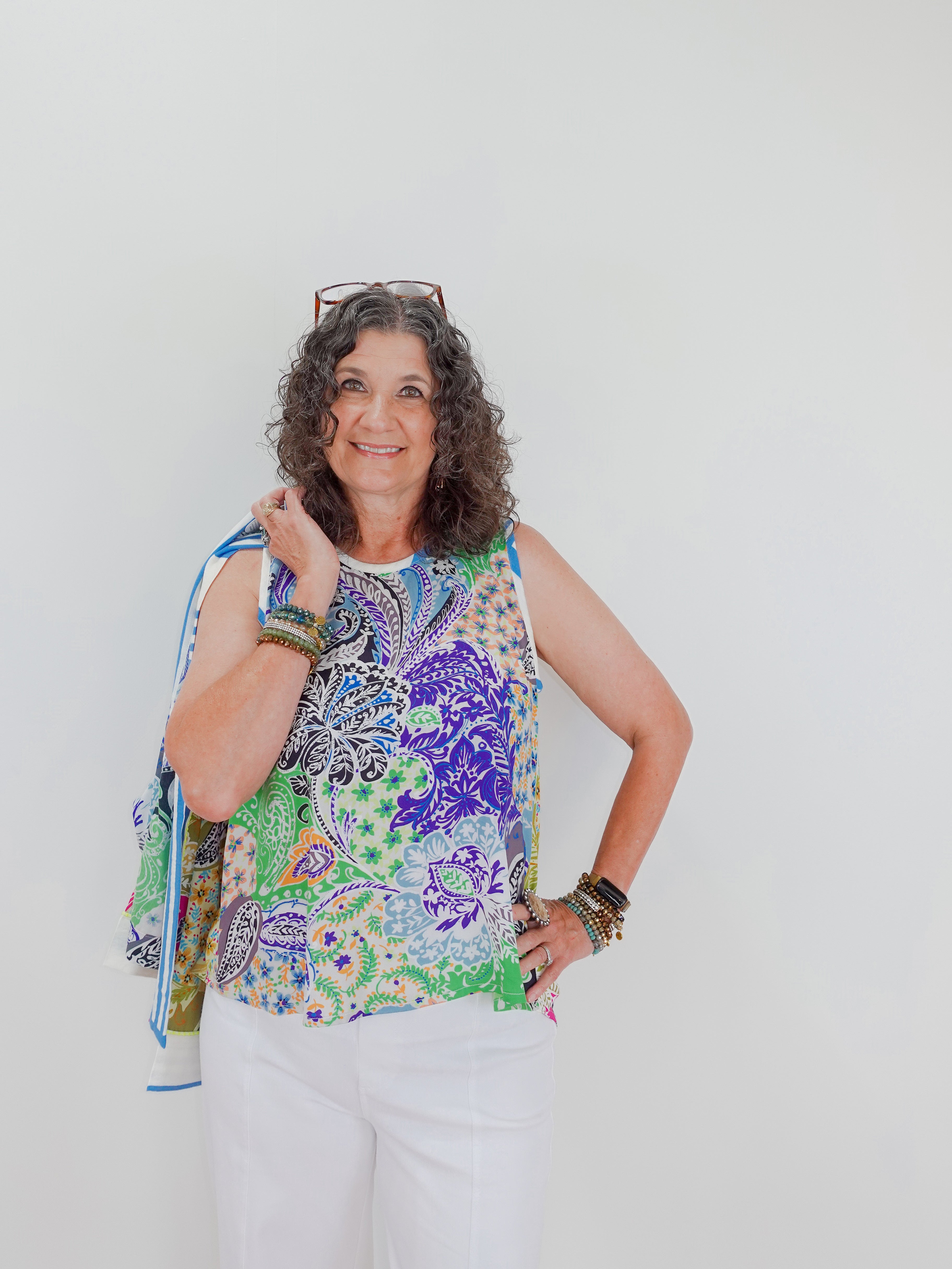 Woman wearing a colorful sleeveless top with a pattern, holding a blue scarf against a white background.