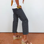Person wearing black and white patterned pants with a white shirt and brown sandals on a red floor.
