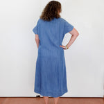 Woman wearing a blue dress standing against a white wall.
