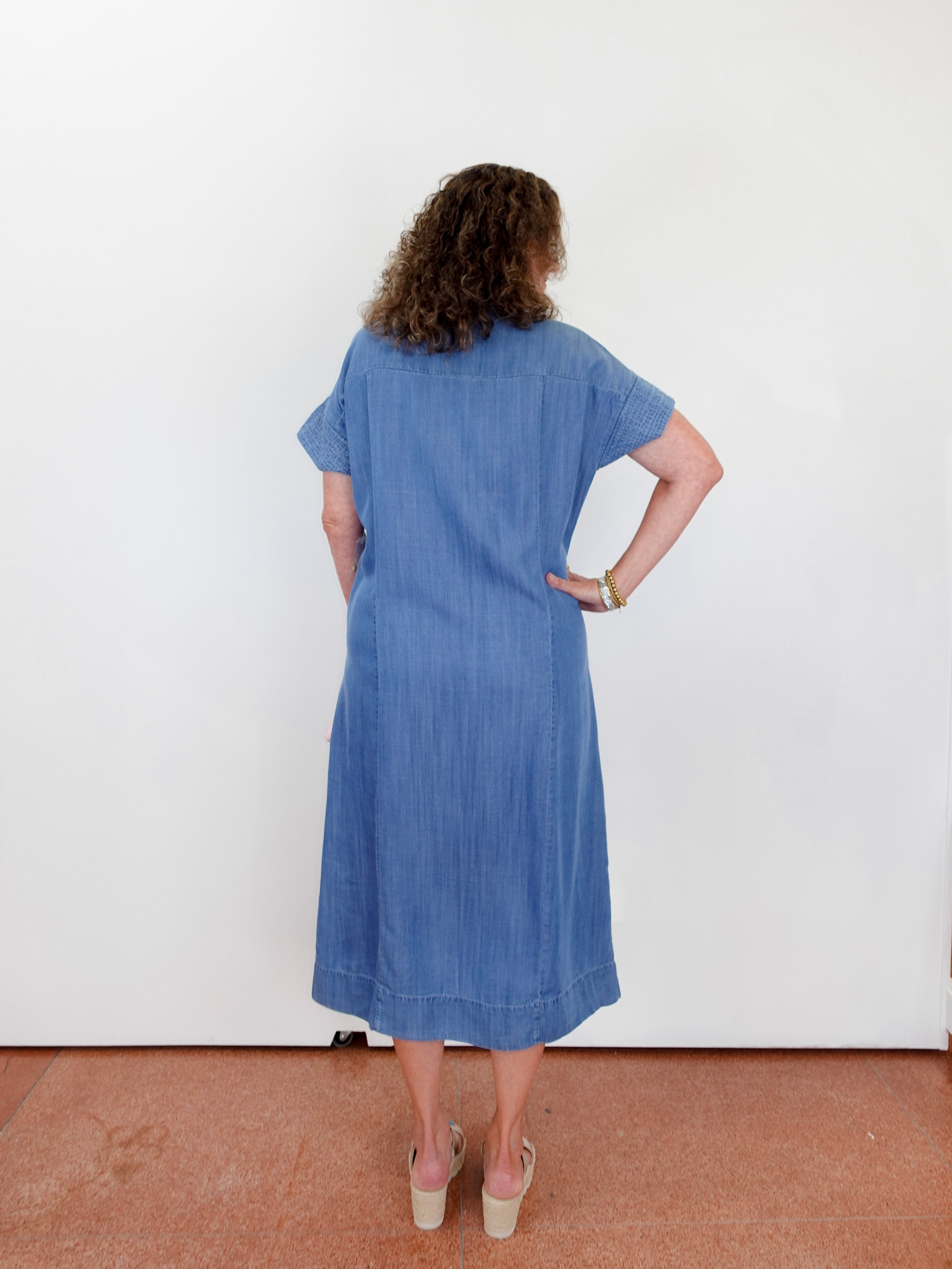 Woman wearing a blue dress standing against a white wall.