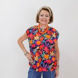 Woman wearing a colorful floral blouse and blue pants against a white background