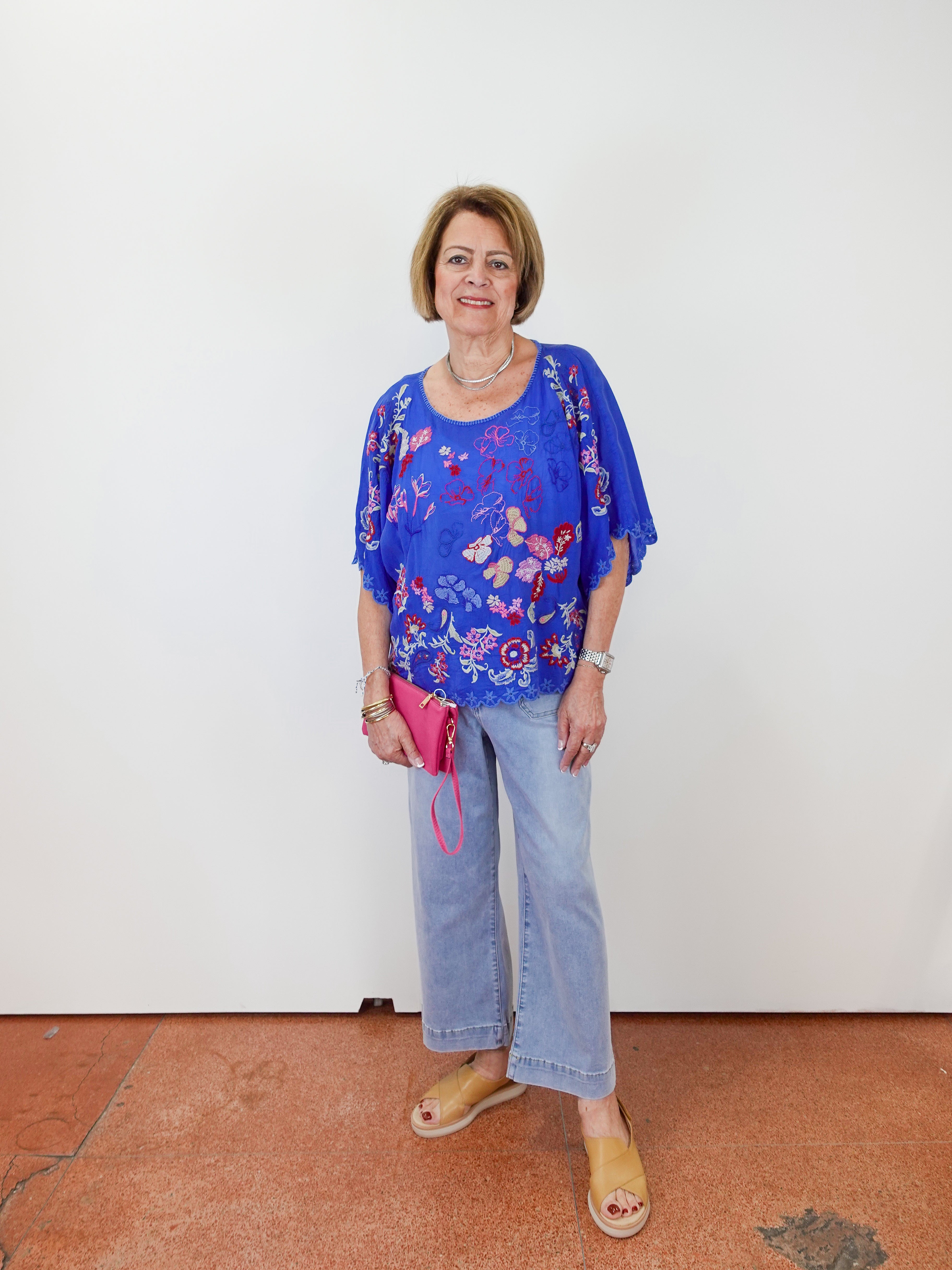 Woman wearing a blue floral blouse and jeans standing against a white wall.