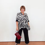 Woman wearing a black and white patterned top with black pants, holding a red handbag against a white background.