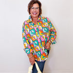 Woman wearing a colorful patterned shirt holding a yellow bag against a white wall.